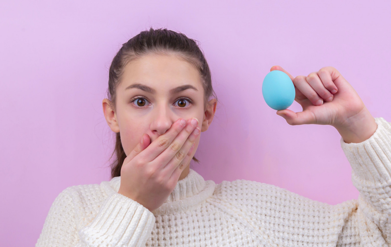 woman in white sweater holding blue egg